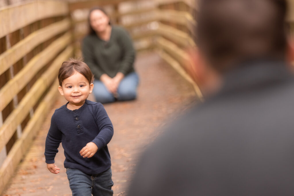 an example of filling the frame in photography: a child running toward their dad who is blurred in front of the camera in the foreground. Mom is sitting on her knees unfocused in the background