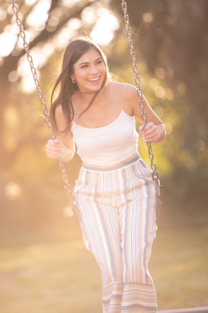 what to wear for senior photos - girl wearing white tank top and stripe pants swinging on a swing