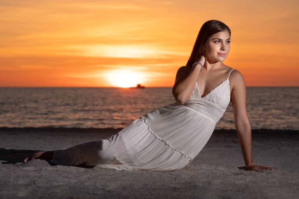 Graduating senior sitting at Sand Key Beach in white dress at sunset