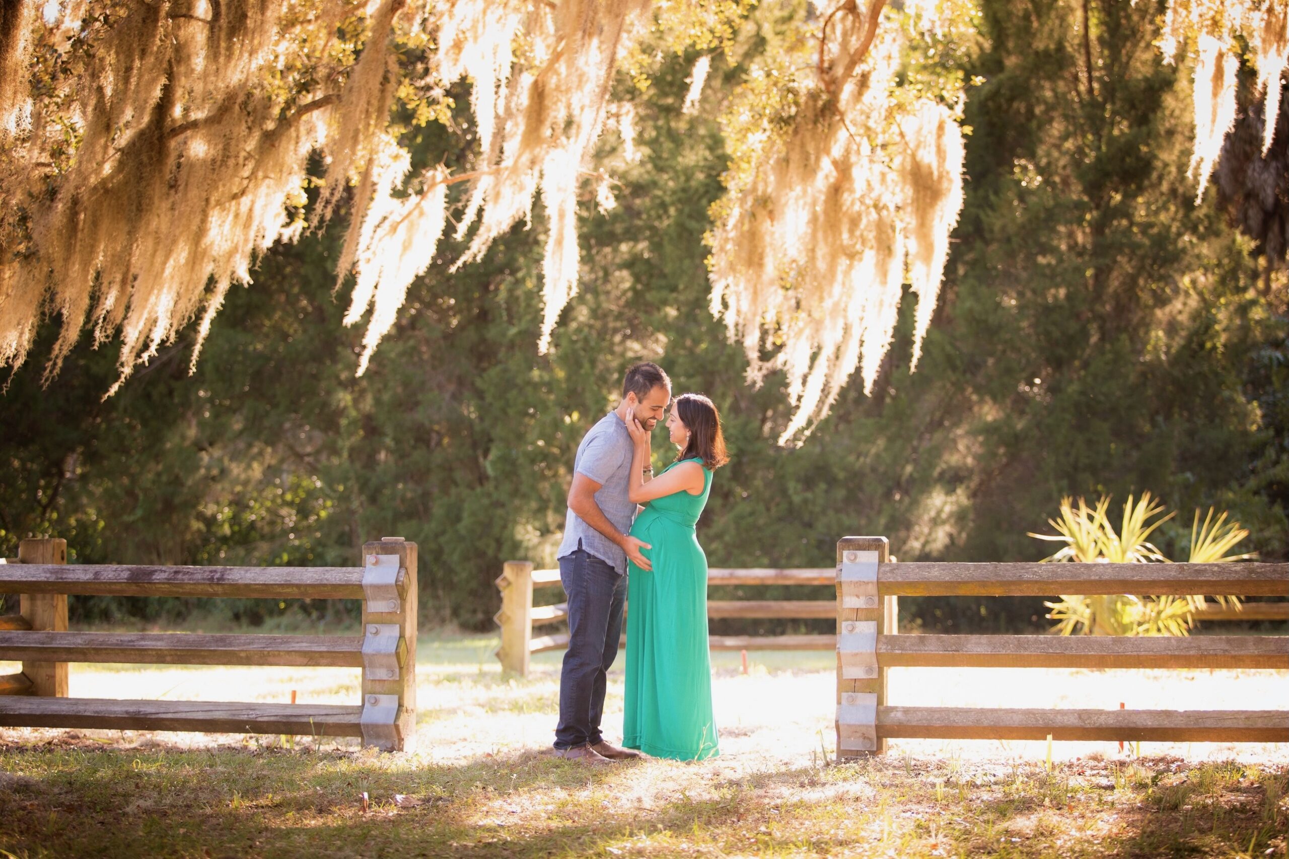 Man leans in to kiss pregnant wife under Spanish moss at Philippe Park in Safety Harbor