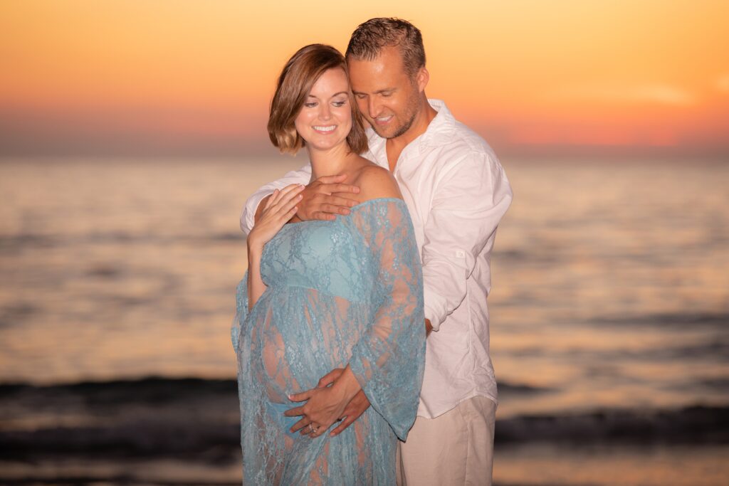 Pregnant woman in light green poses on Sand Key Beach at sunset