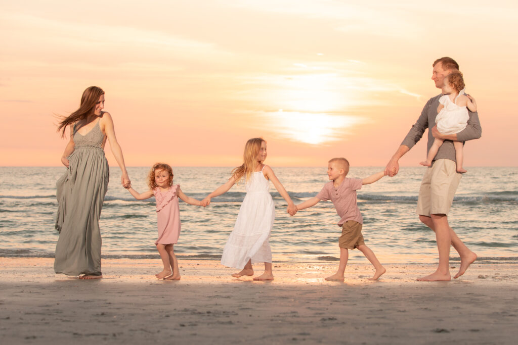 Family of 6 hold hands walking in water at Clearwater Beach in family photoshoot outfit