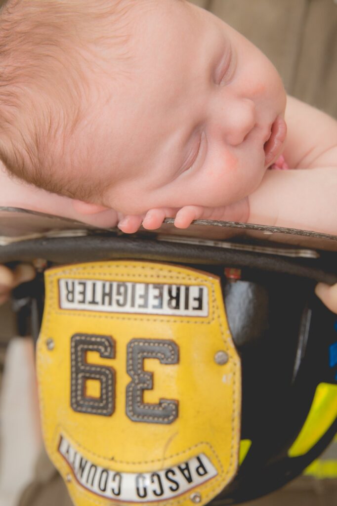 newborn photos of baby lying on firefighter helment