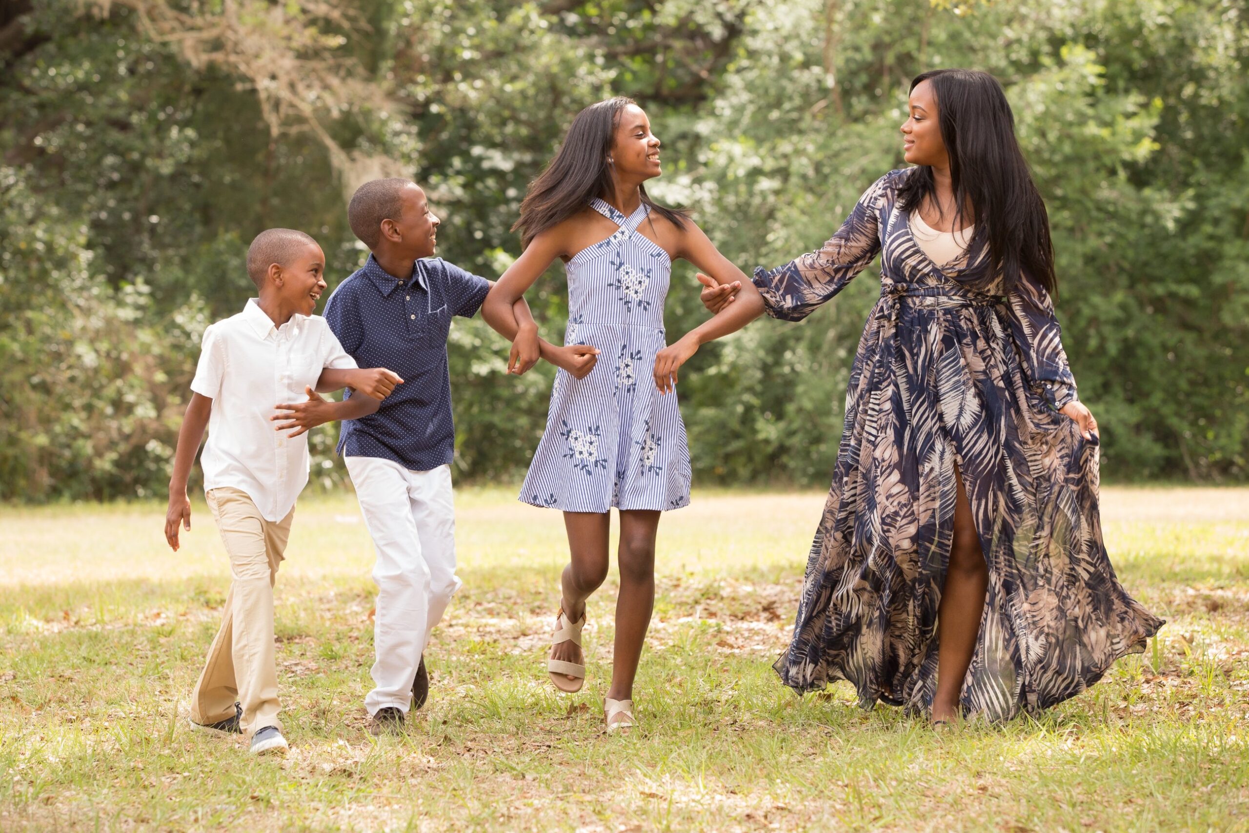 black woman and her 3 young kids skipping through a field - ideas for celebrating Mother's Day