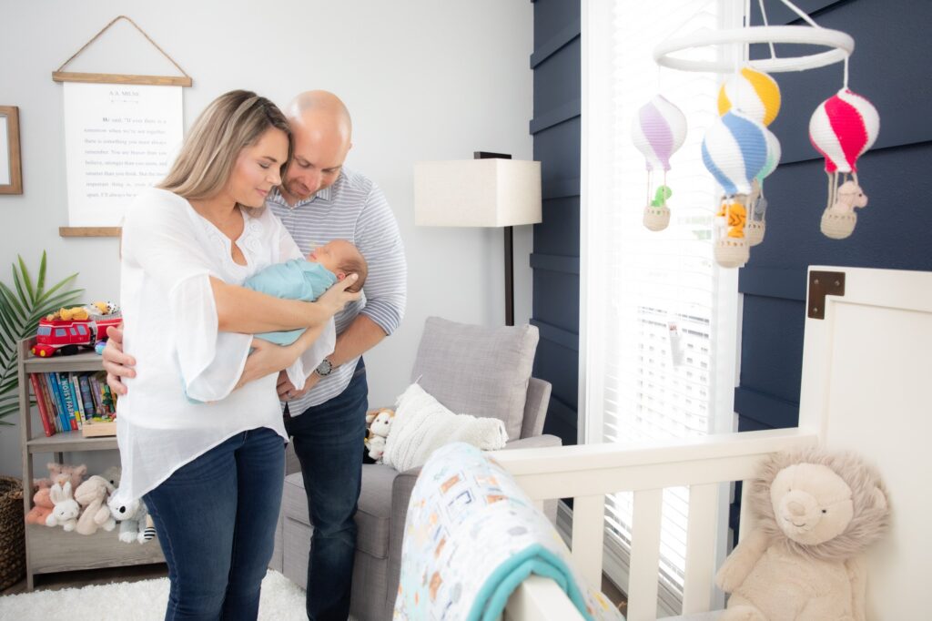 parents in bedroom holding their newborn baby next to window and crib