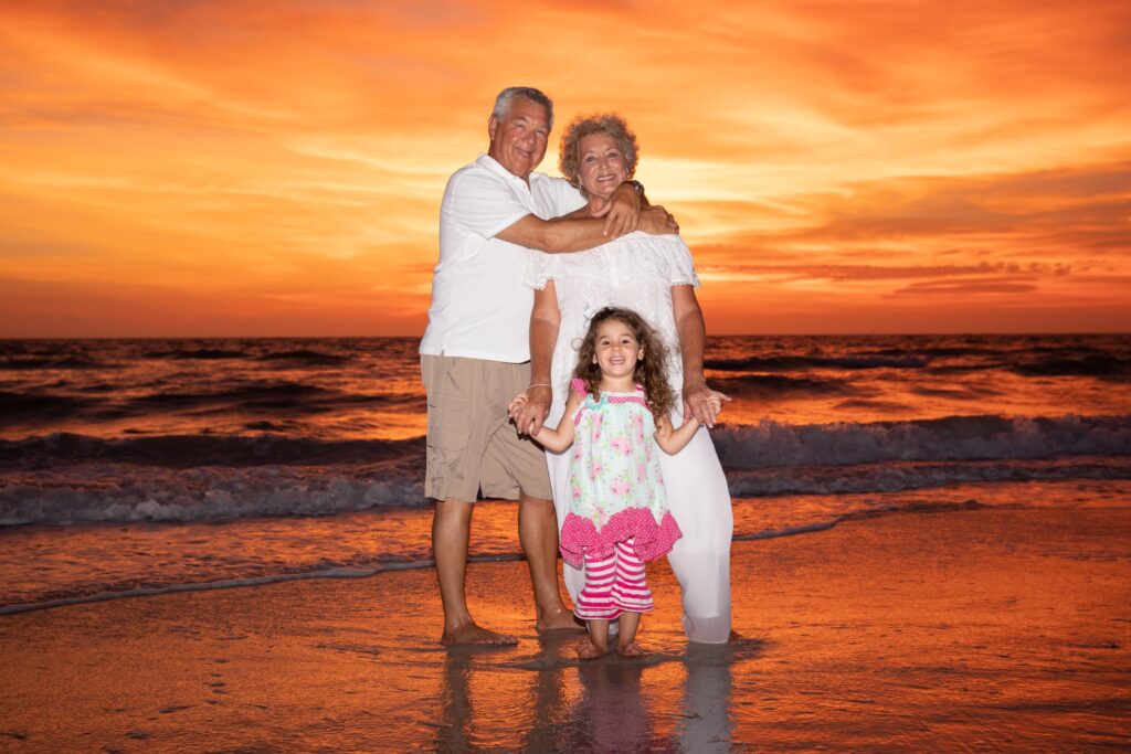 young girl taking pictures with her grandparents on a Florida beach during sunset