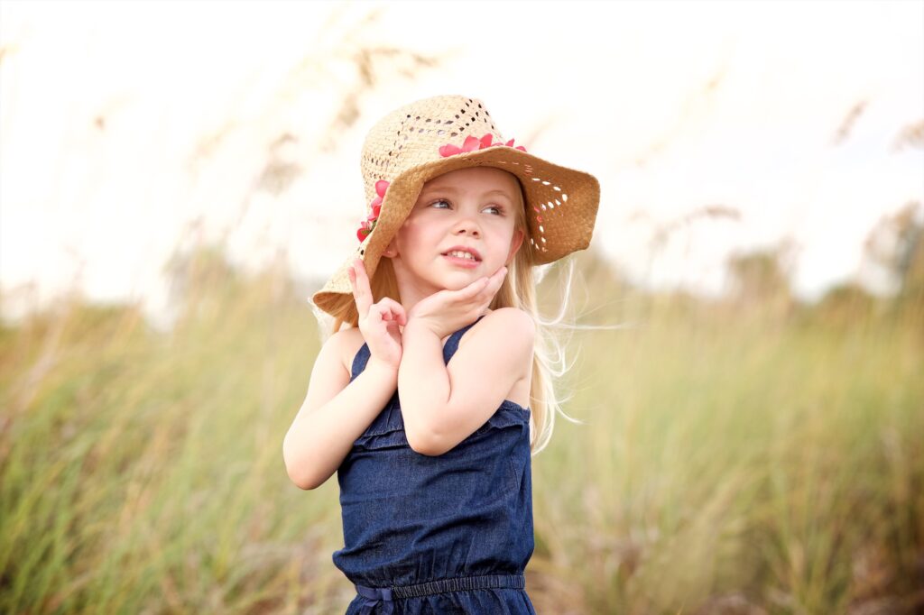 small blonde girl holding hat over her ears posing for pictures on Sand Key Beach near Tampa