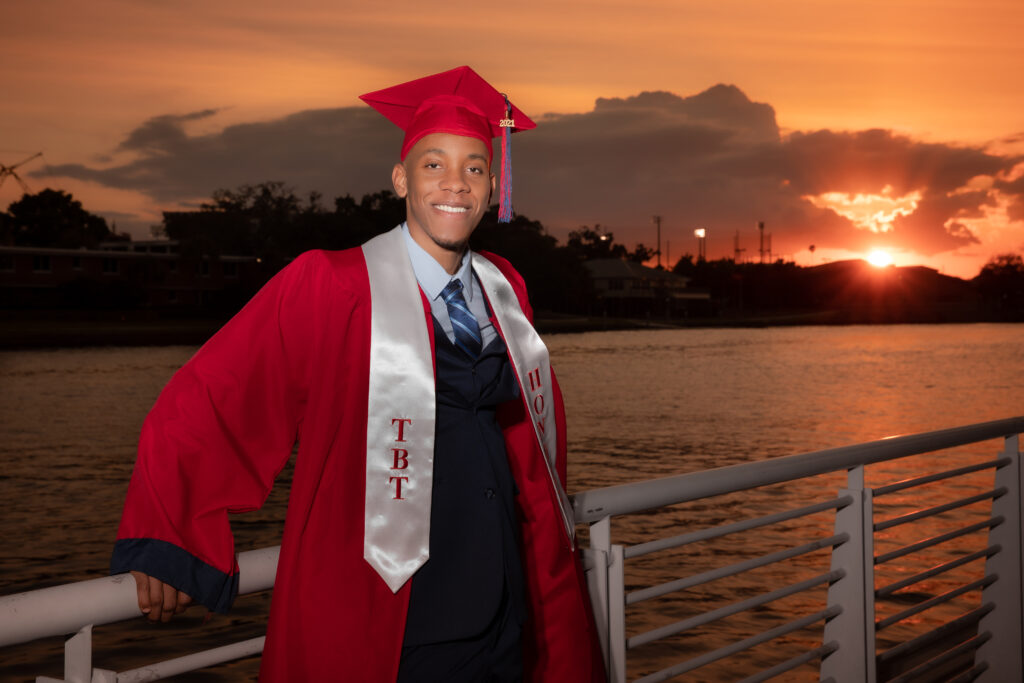 guy in red cap in gown in front of Tampa sunset for senior pictures