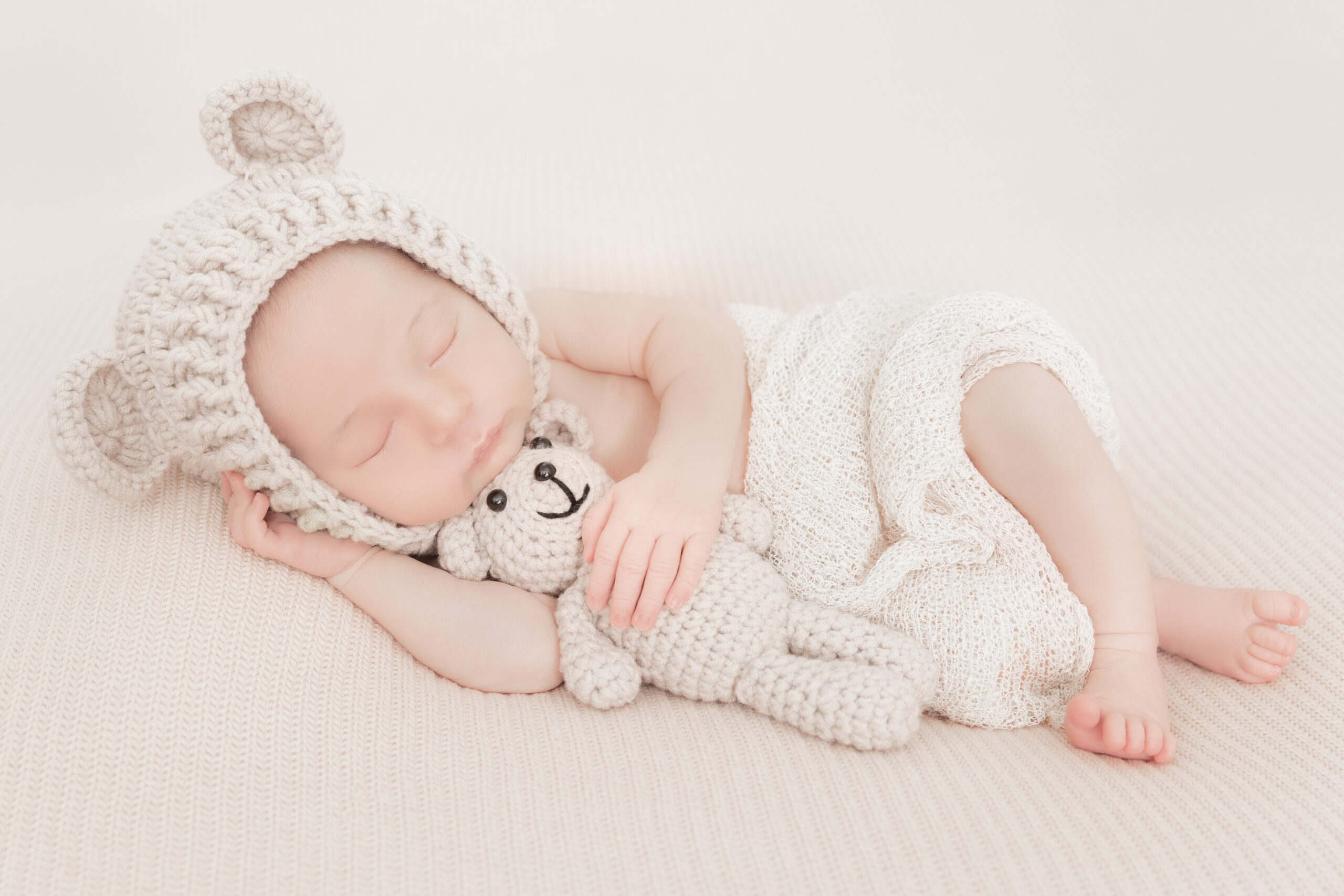 Newborn baby with knitted cap holding teddy bear