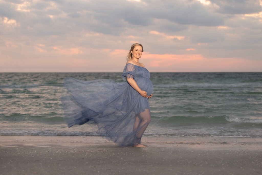 Pregnant woman in blue dress blowing in the wind on beach