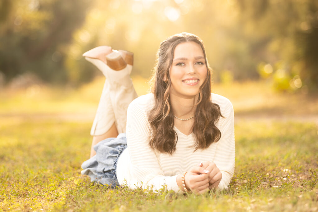 poses for pictures: girl lying on stomach in grass with cowboy boots kicked up behind her 