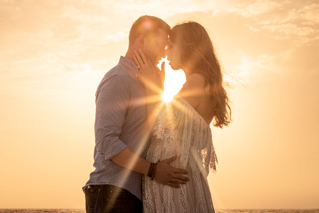 After proposal man and woman embrace with sun behind them on St. Pete Beach at sunset