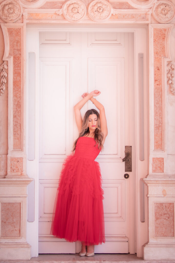 poses for pictures: woman in red dress raising both of her hands above her head and crossing them