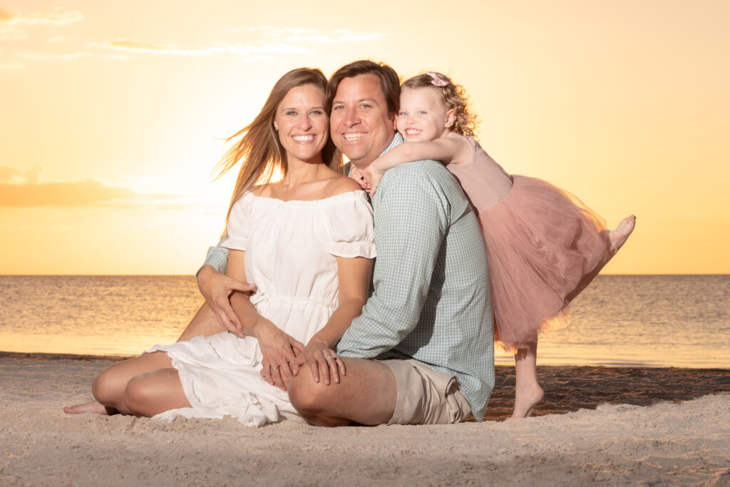 Family posing with daughter kicking her leg up at Howard Park Beach in Tarpon Springs