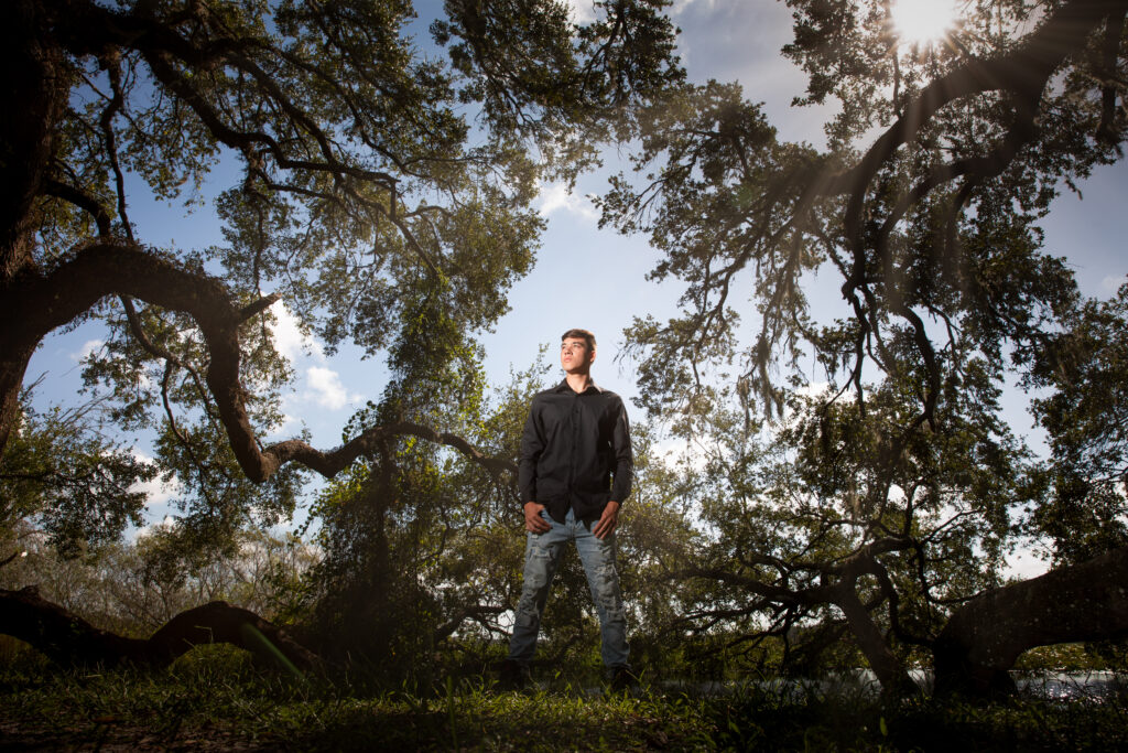 high school senior wearing jeans and a button down in a forest for senior photos