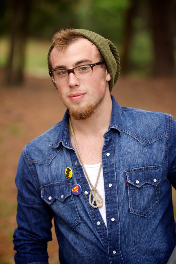 senior outfit ideas for guys - red head wearing beanie, glasses, denim shirt, and DC buttons