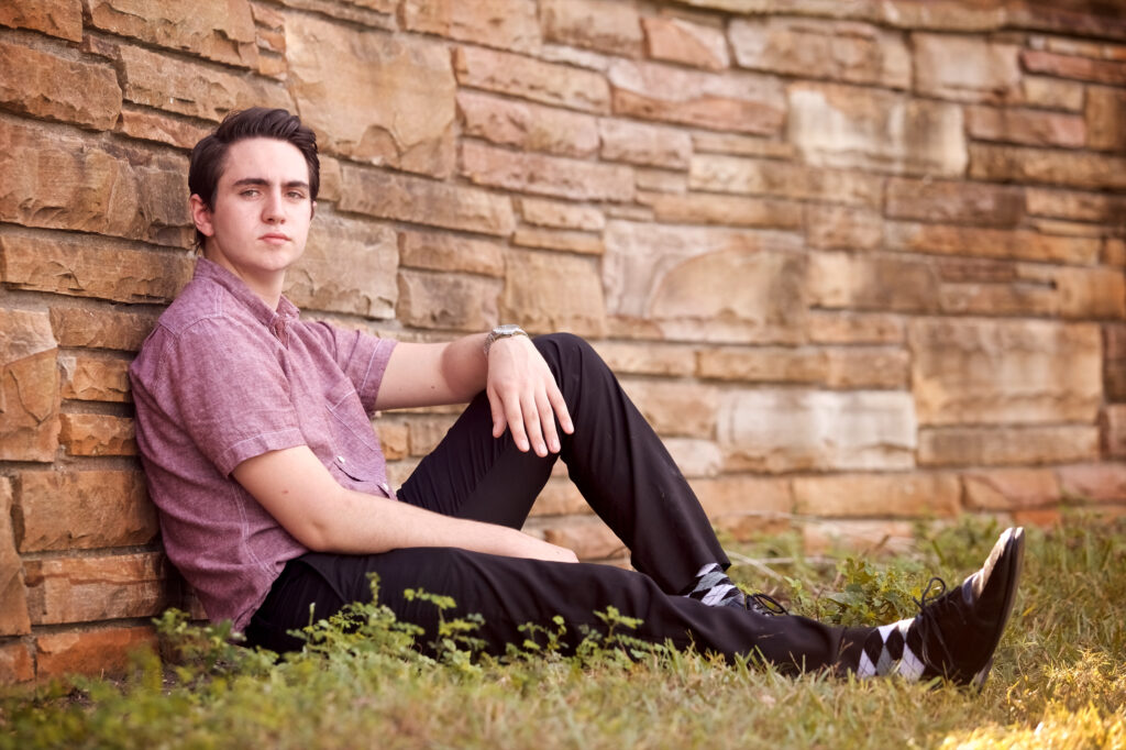 poses for guy senior pictures: Sit on the ground, and prop your back leg (the one furthest from the camera) up.  Place your back arm on the edge of your knee and let it hand. Put your front leg straight and drape the front arm over your knee until it hangs in between your legs. You can choose to lean against a brick wall or fence if it's more comfortable. 