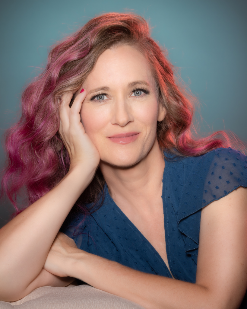 woman over 40 with pink/purple hair, wearing a nice blue blouse for her 40-over-40 photography shoot