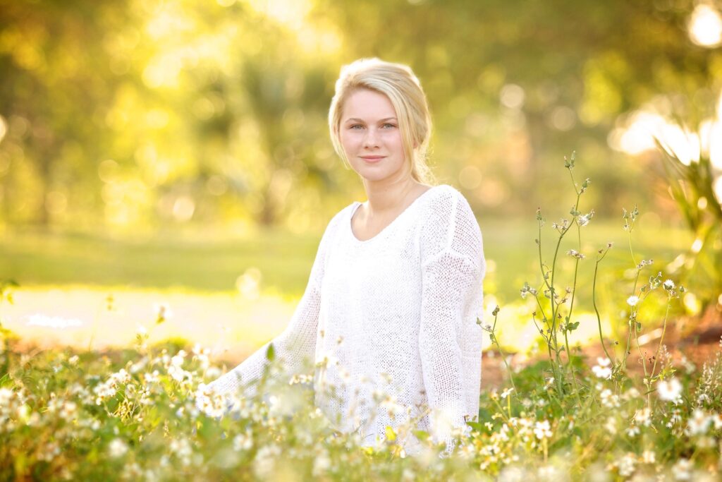 blonde girl in a white top sitting a field of flowers for a gorgeous summer photo shoot