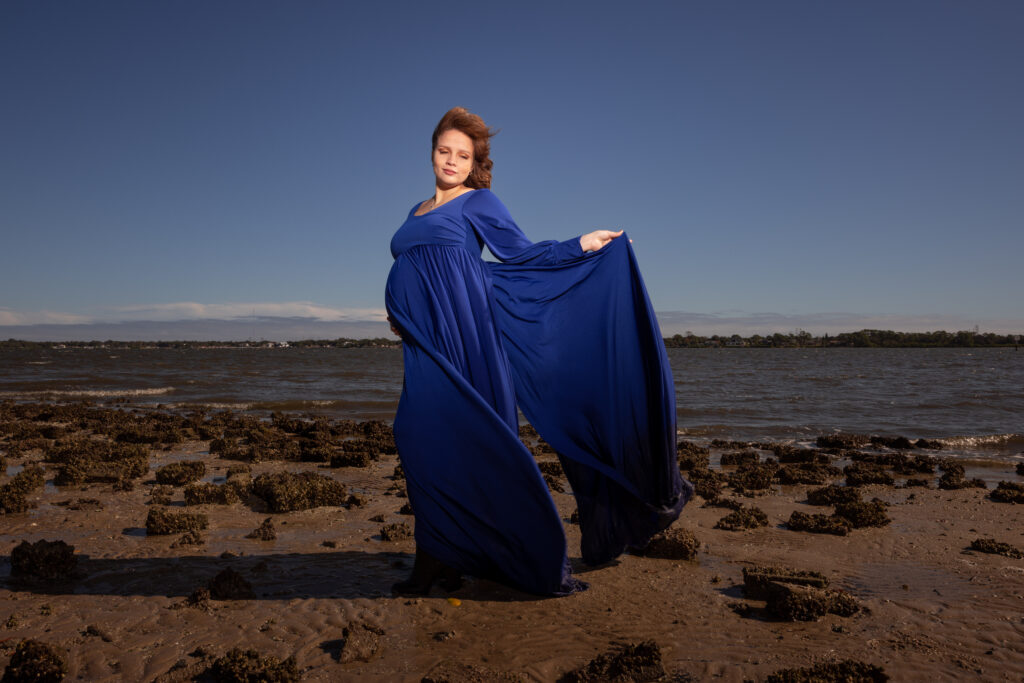 maternity photoshoot outfit: woman wears full-length, bold blue dress for her photos in at the beach