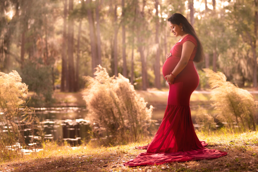 maternity photoshoot outfit: woman wears full-length, bold red dress for her photos in a whimsical Florida park