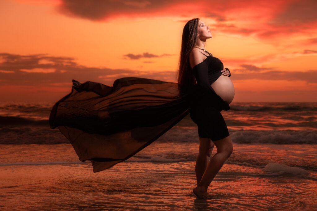 maternity photoshoot outfit ideas: woman wears a black sheer dress on the beach 
