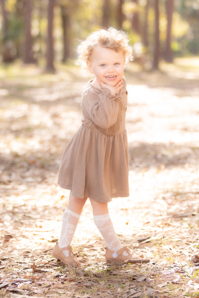little girl in a brown dress walking through a field, smiling at the camera during a candid photography shot