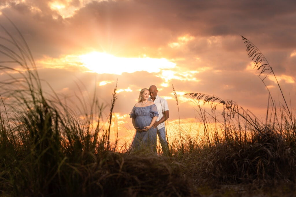 Maternity ouple stand behind seagrass in beach sunset portrait