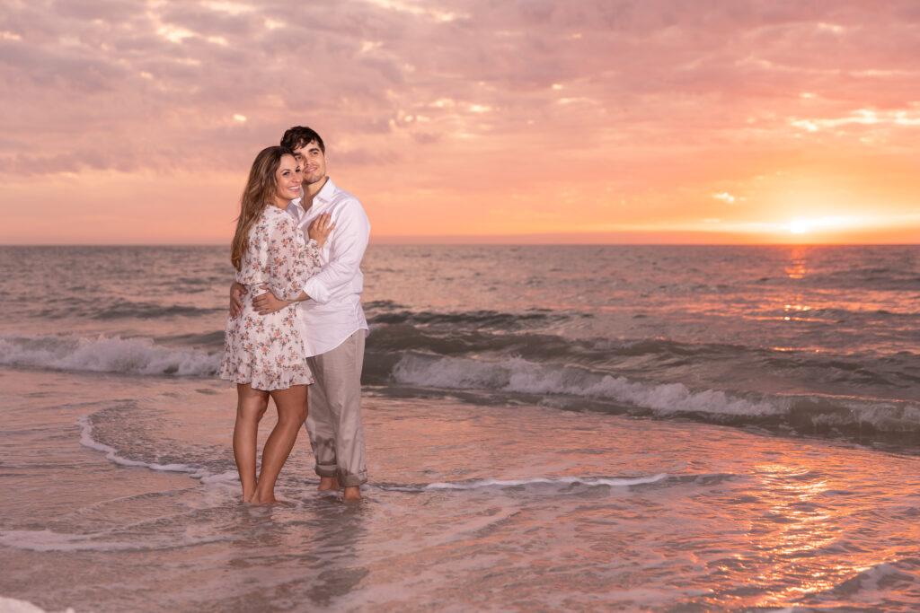 happy engaged couple in water hugging at sand key beach at sunset
